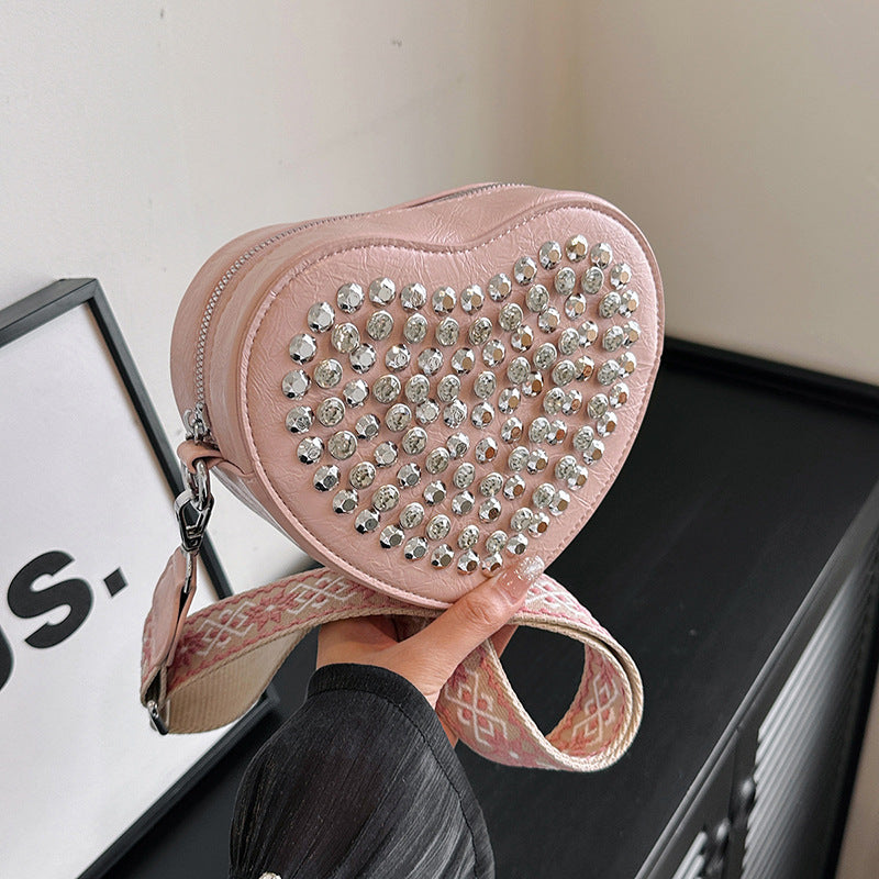 Hjerteformet taske med bred skulderrem i westernstil, der matcher nitter og som crossbody-telefontaske