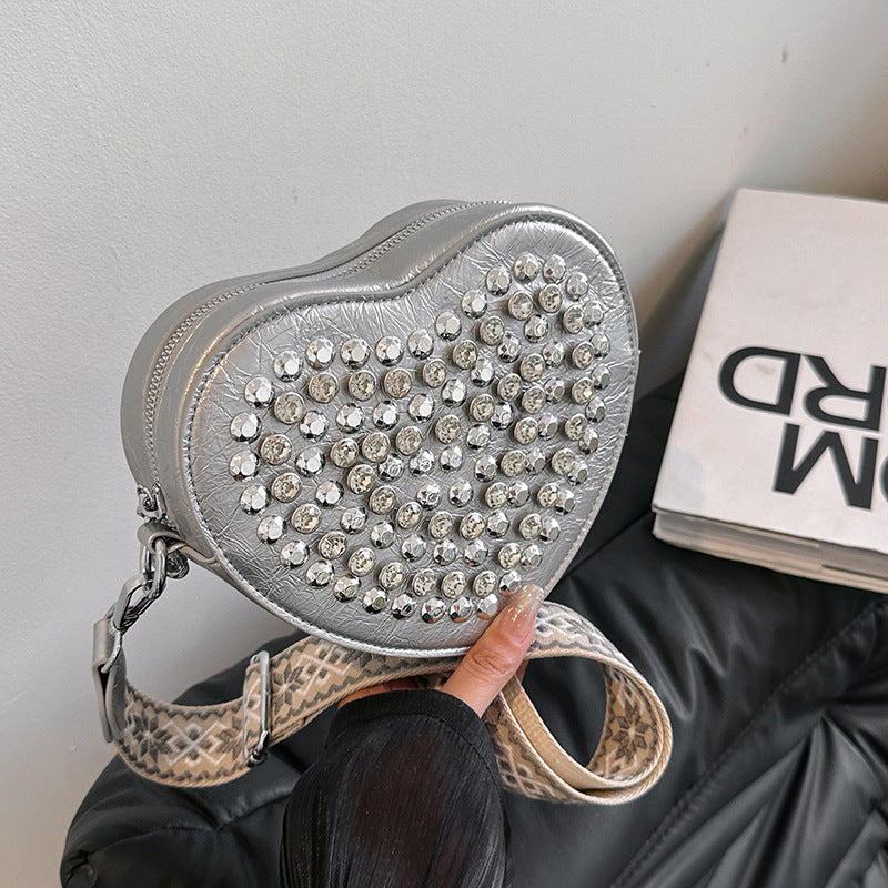 Hjerteformet taske med bred skulderrem i westernstil, der matcher nitter og som crossbody-telefontaske