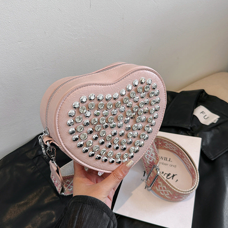 Hjerteformet taske med bred skulderrem i westernstil, der matcher nitter og som crossbody-telefontaske